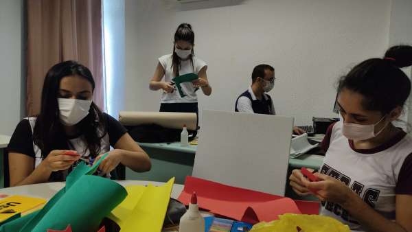 Fotografia de quatro pessoas sentadas ao redor de uma mesa recortando papeis.