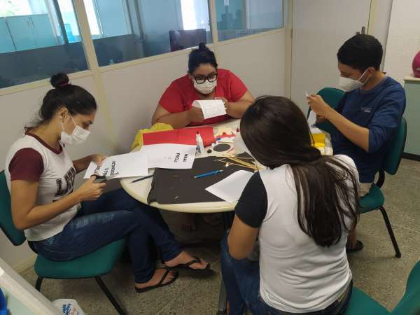 Fotografia de quatro pessoas sentadas ao redor de uma mesa recortando papeis.
