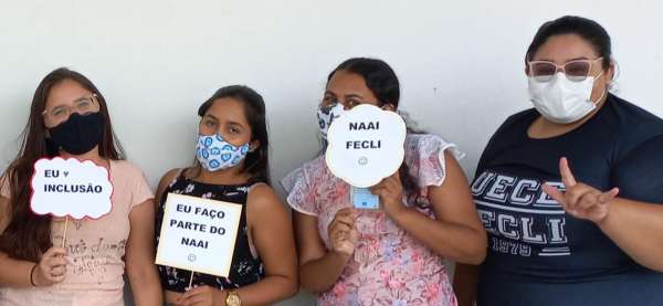 a imagem mostra quatro mulheres de pé, vistas da cintura pra cima, segurando plaquinhas qu dizem "NAAI-FECLI" "EU FAÇO PARTE DO NAAI"