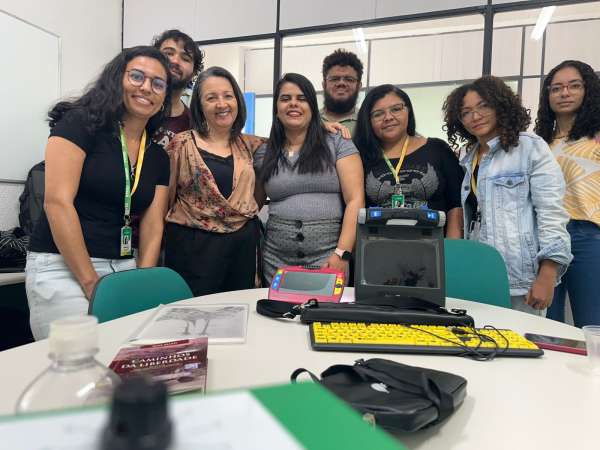 #PraTodosVerem A foto mostra as coordenadoras Marisa Aderaldo (NAAI) e Estrela (SDHCE), ladeadas por parte de suas respectivas equipes. Com destaque, à frente da mesa, estão algumas ferramentas assistivas para auxílio de pessoas com deficiência visual.